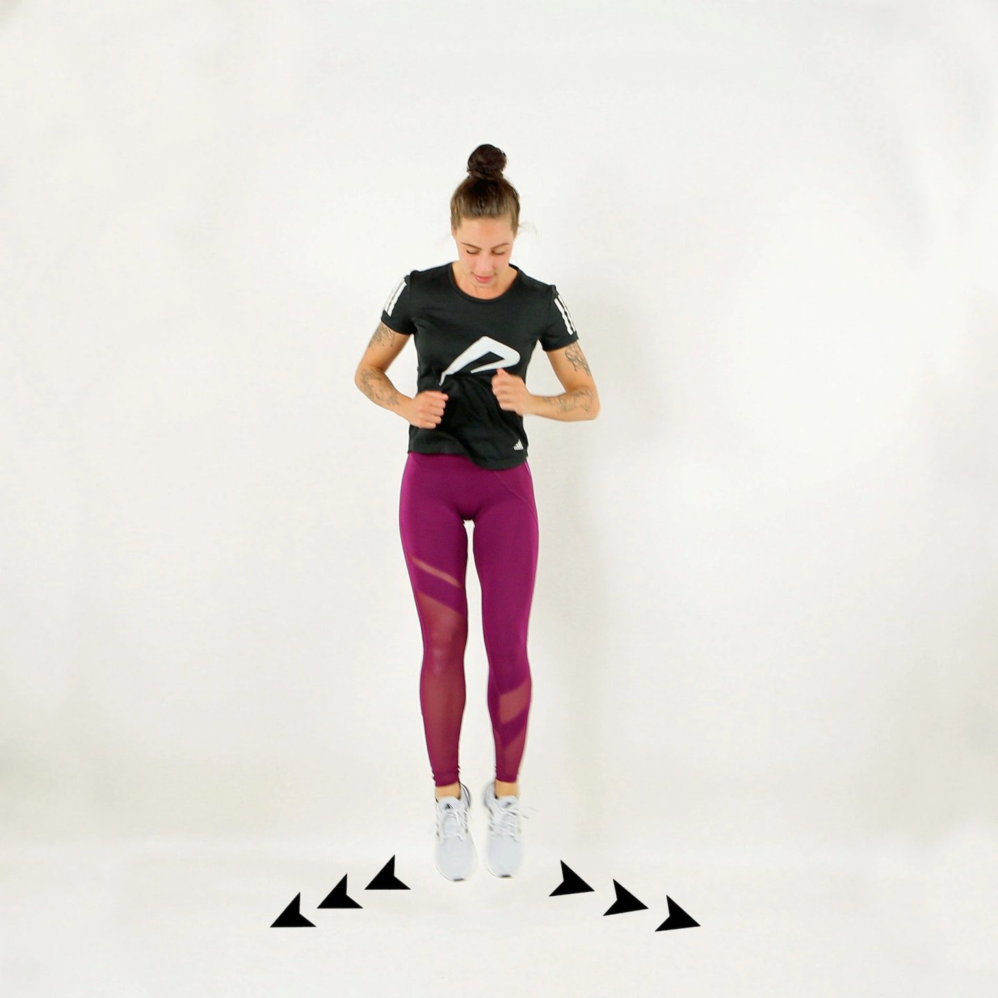 Woman mid-air performing a lateral agility jump drill wearing a black Adidas running top, purple mesh leggings and white trainers.