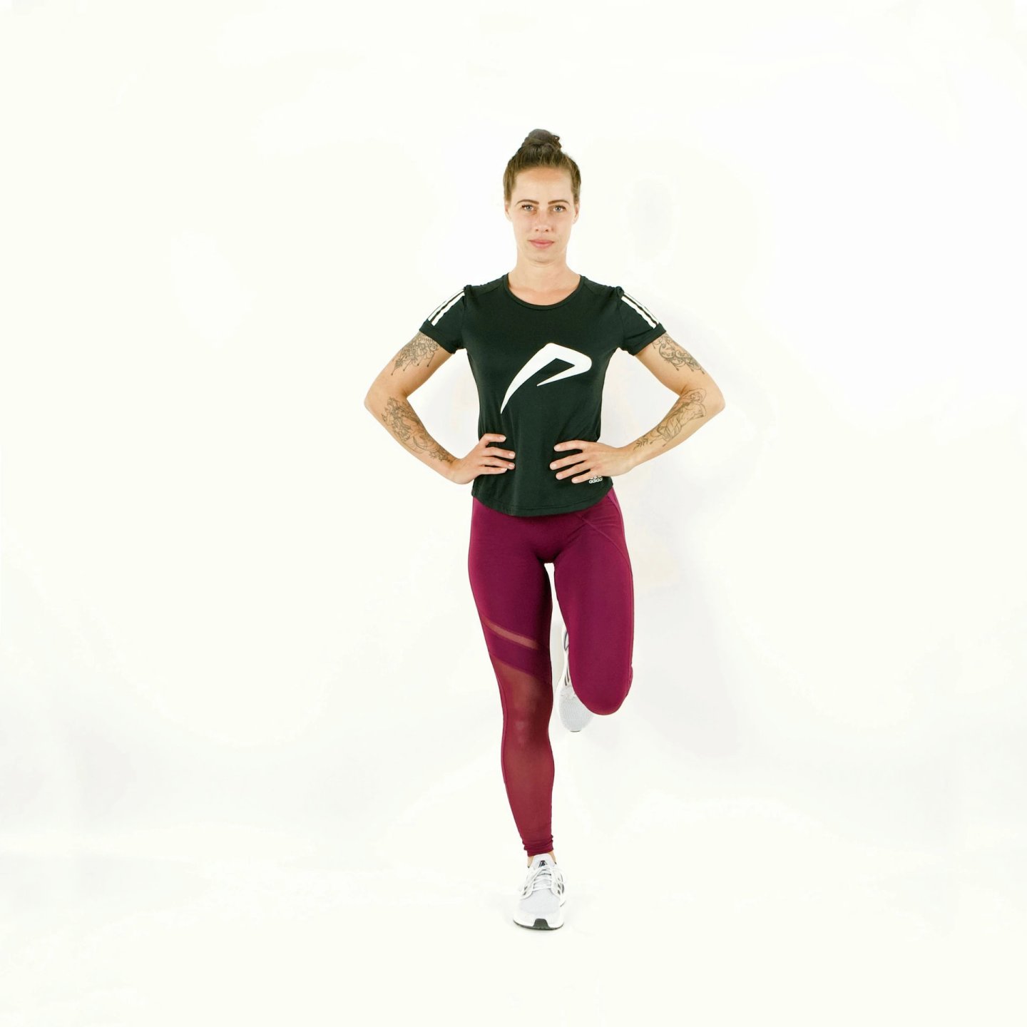 Female runner in burgundy leggings and black tee performing a forward lunge drill with hands on hips, white background.