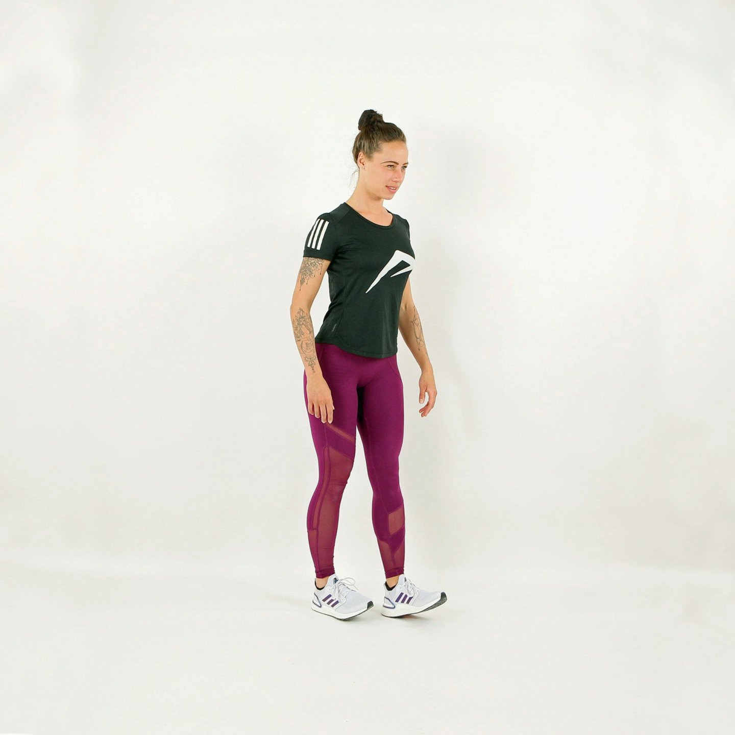 Woman wearing magenta full-length running tights with mesh panel detailing, paired with a dark green Adidas running tee and white trainers.