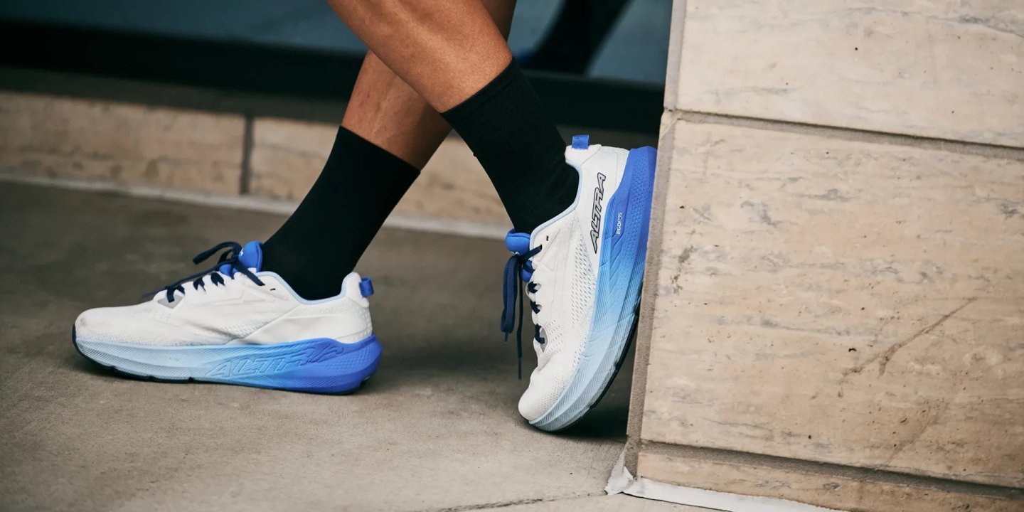 Man wearing Altra FWD Via 2 running shoes in white and blue gradient colorway, seated on concrete steps