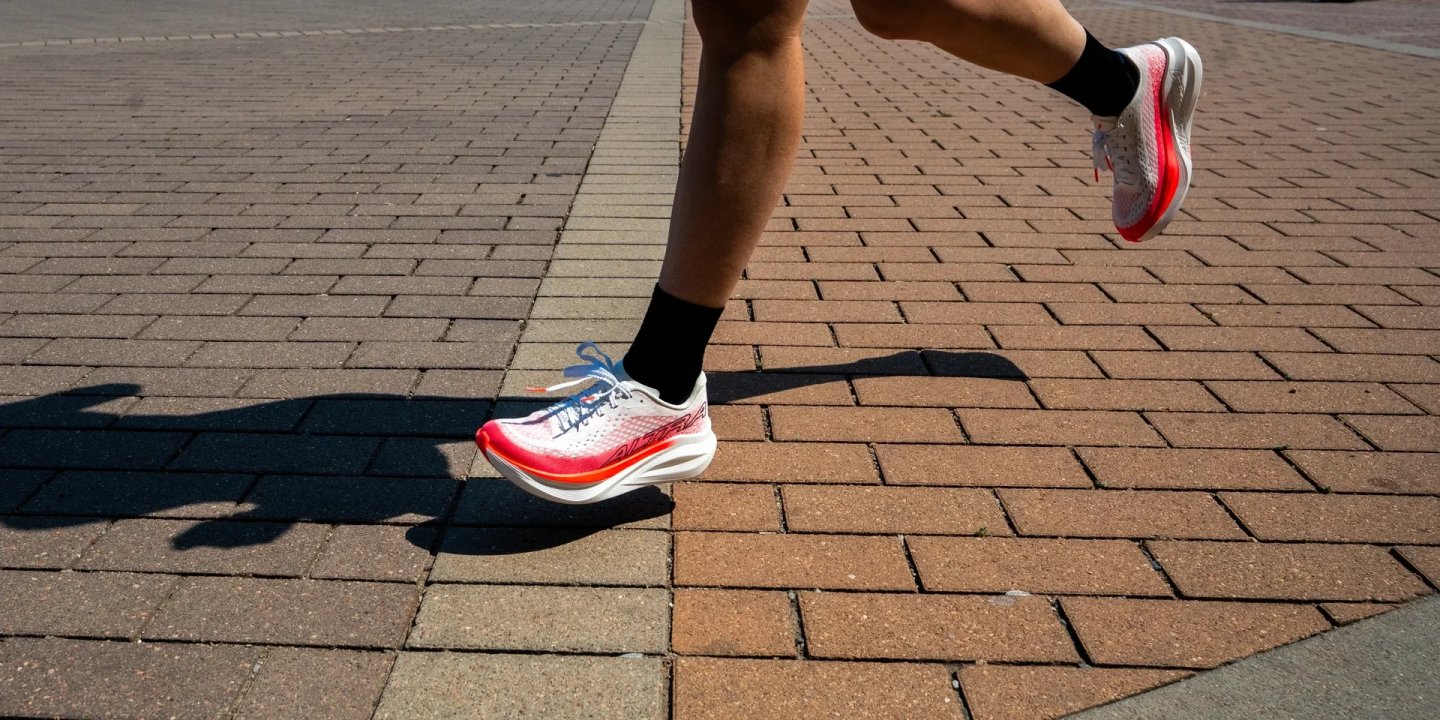 Runner in Altra Vanish Tempo shoes in white and red sprinting across a brick paved surface in bright sunlight.