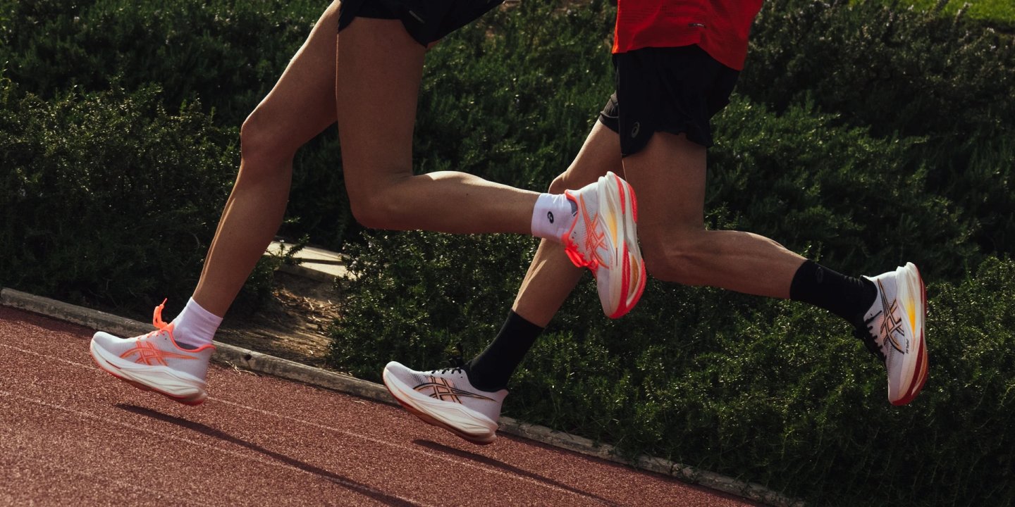 Two runners on a red athletics track wearing ASICS Sonic Blast 2 Ignite shoes in white and coral colourway.