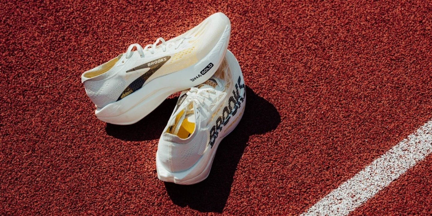 Brooks Hyperion Elite 6 running shoes in white and gold with DNA Gold midsole, placed on a red athletics track.