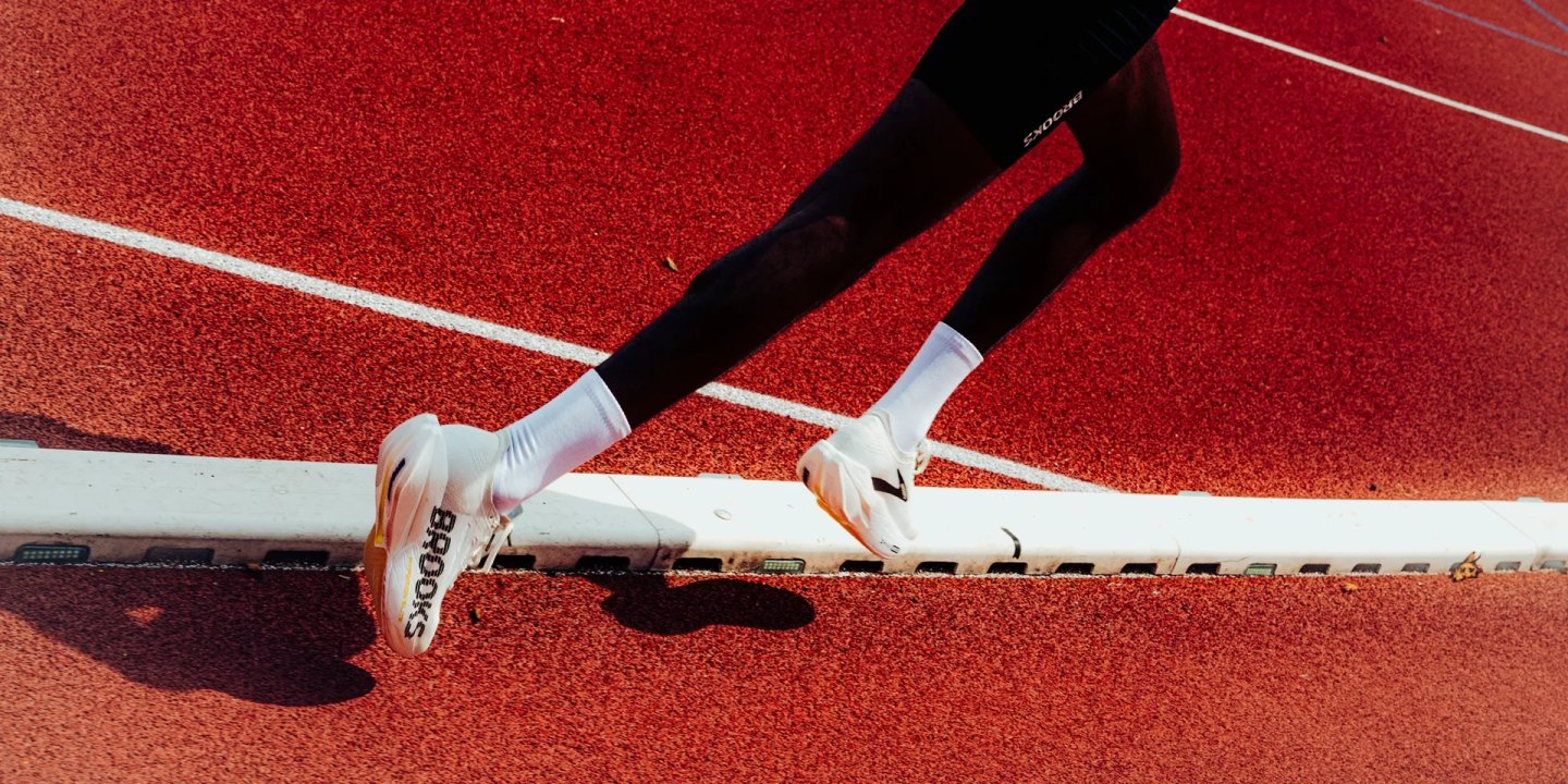 Runner wearing Brooks Hyperion Elite 6 racing shoes and Brooks tights mid-stride on a red athletics track