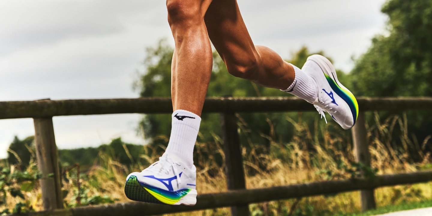 Runner mid-stride wearing white Mizuno Hyperwarp running shoes with blue and neon yellow accents, paired with Mizuno socks