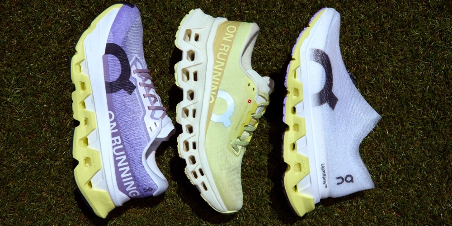 Three On Cloudmonster 3 running shoes in purple, yellow, and white colorways laid side by side on grass