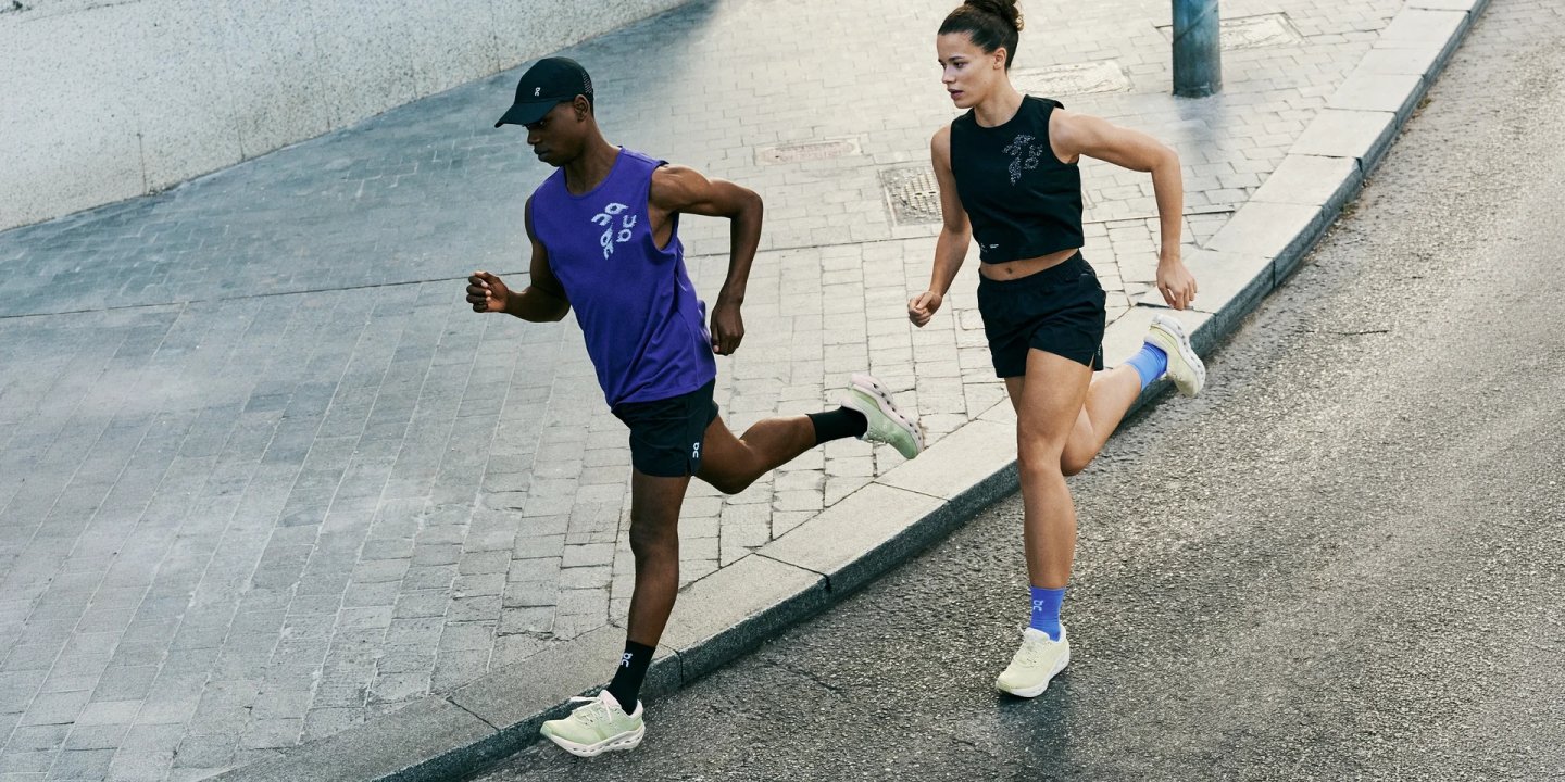Man and woman running on city cobblestone pavement wearing On Cloudrunner 3 shoes in mint, with On running apparel.