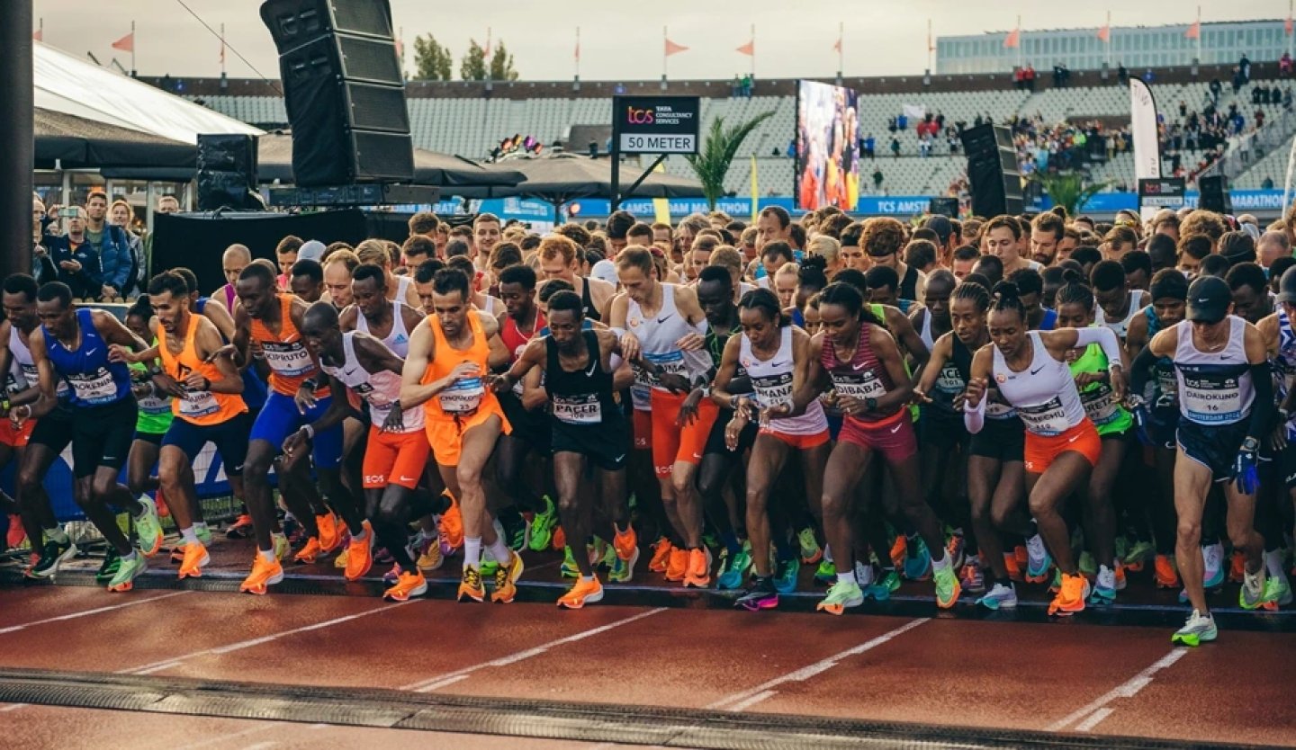 Hundreds of elite and competitive runners bursting from the start line at the TCS Amsterdam Marathon inside the Olympic Stadium.
