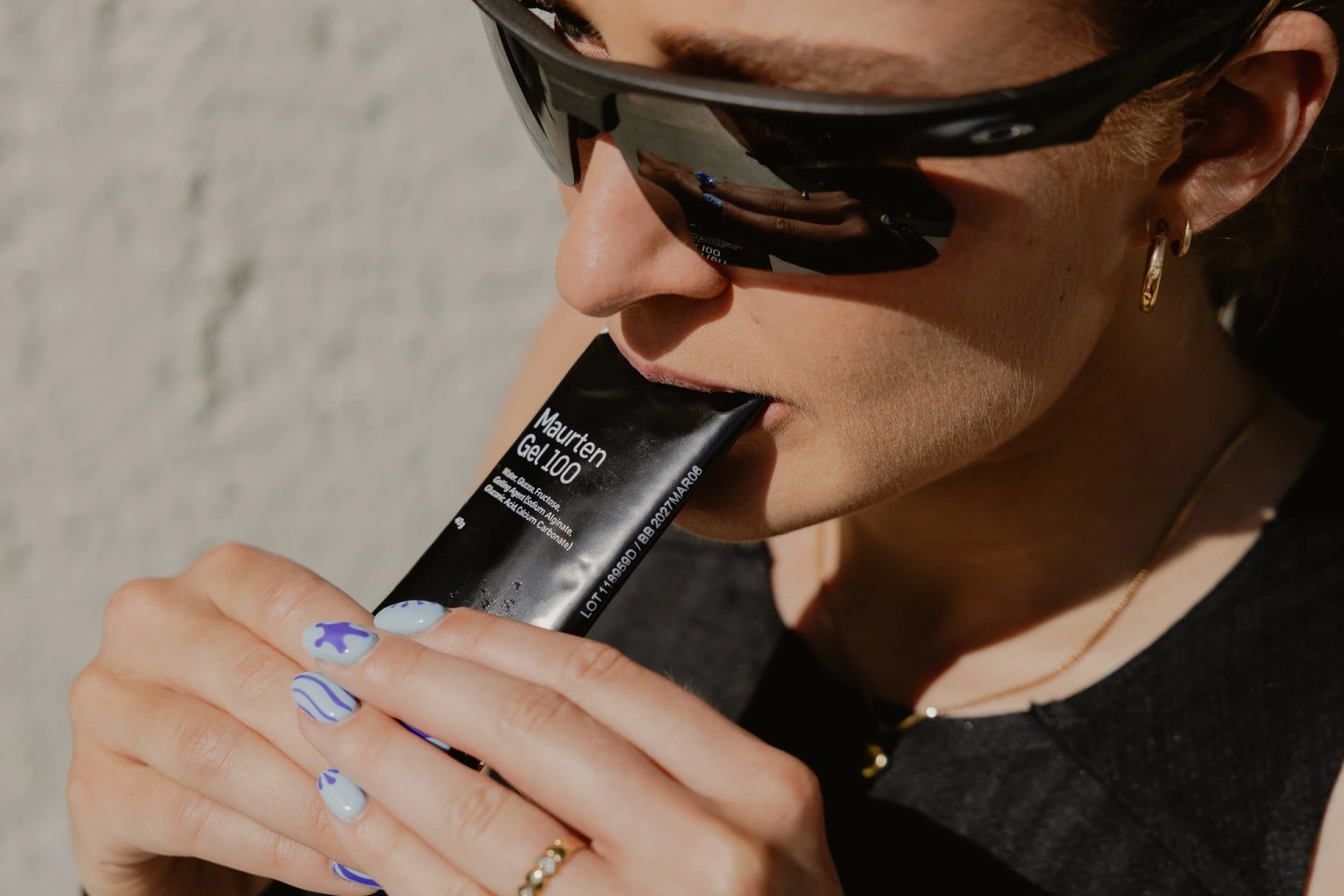 Female runner in sport sunglasses consuming a Maurten Gel 100 energy gel sachet during a run