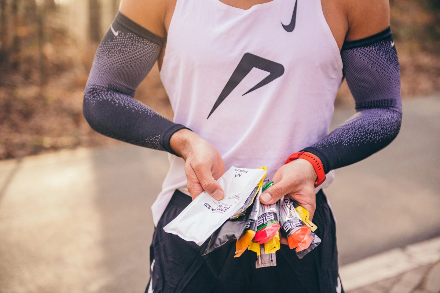 Runner in Nike vest and compression arm sleeves holding Maurten Drink Mix 320 sachets and SiS GO energy gels before a run