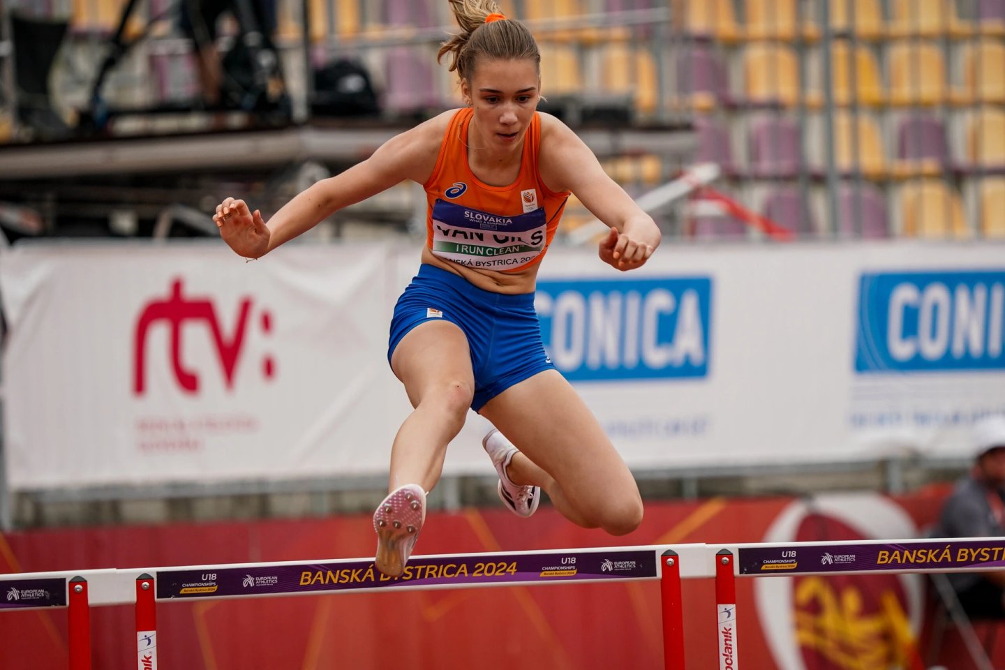 Athlete Zoe Van Gils in orange Netherlands vest clears a hurdle during 400m hurdles semi-final at Banská Bystrica 2024 U18 Championships