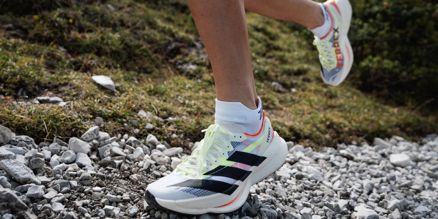Runner wearing adidas Terrex trail shoes in white and neon yellow on a rocky gravel mountain path.