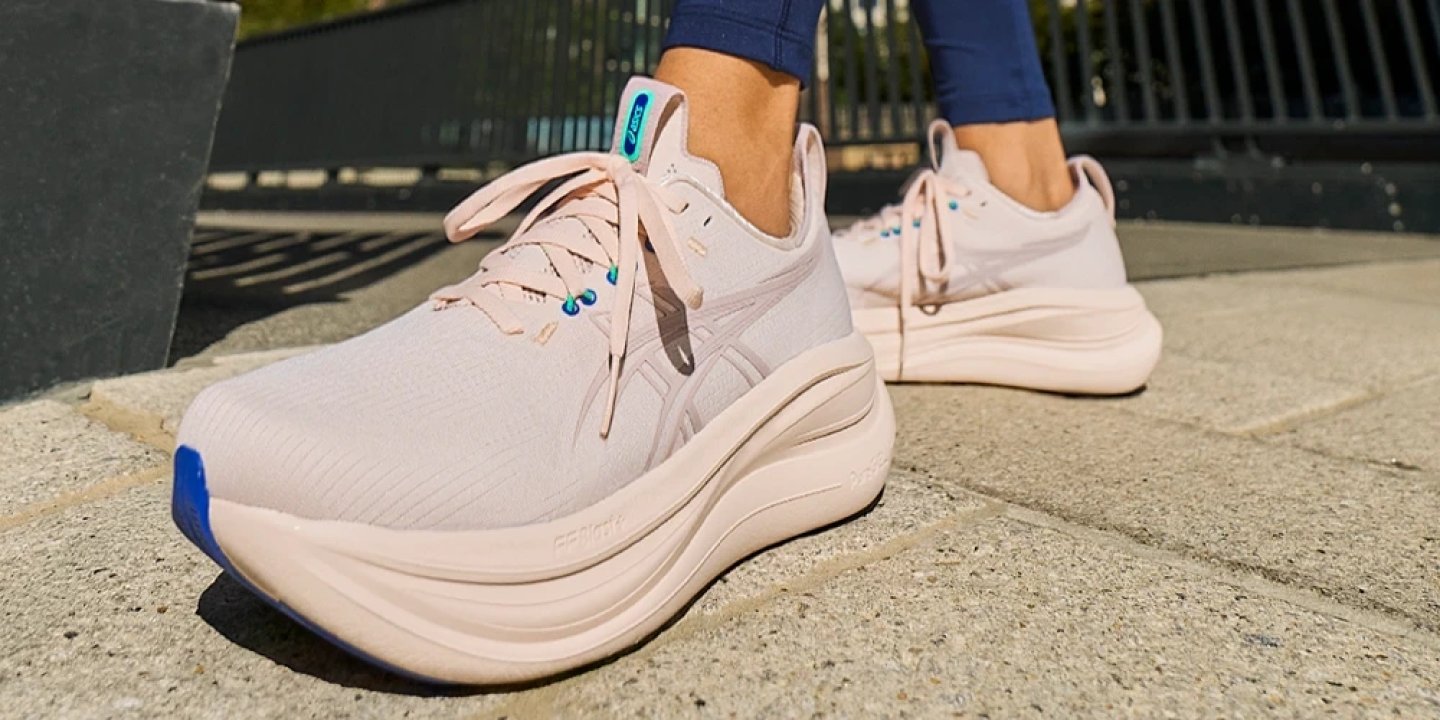 Woman wearing ASICS Gel-Nimbus 27 running shoes in pale pink with blue outsole accent on stone steps
