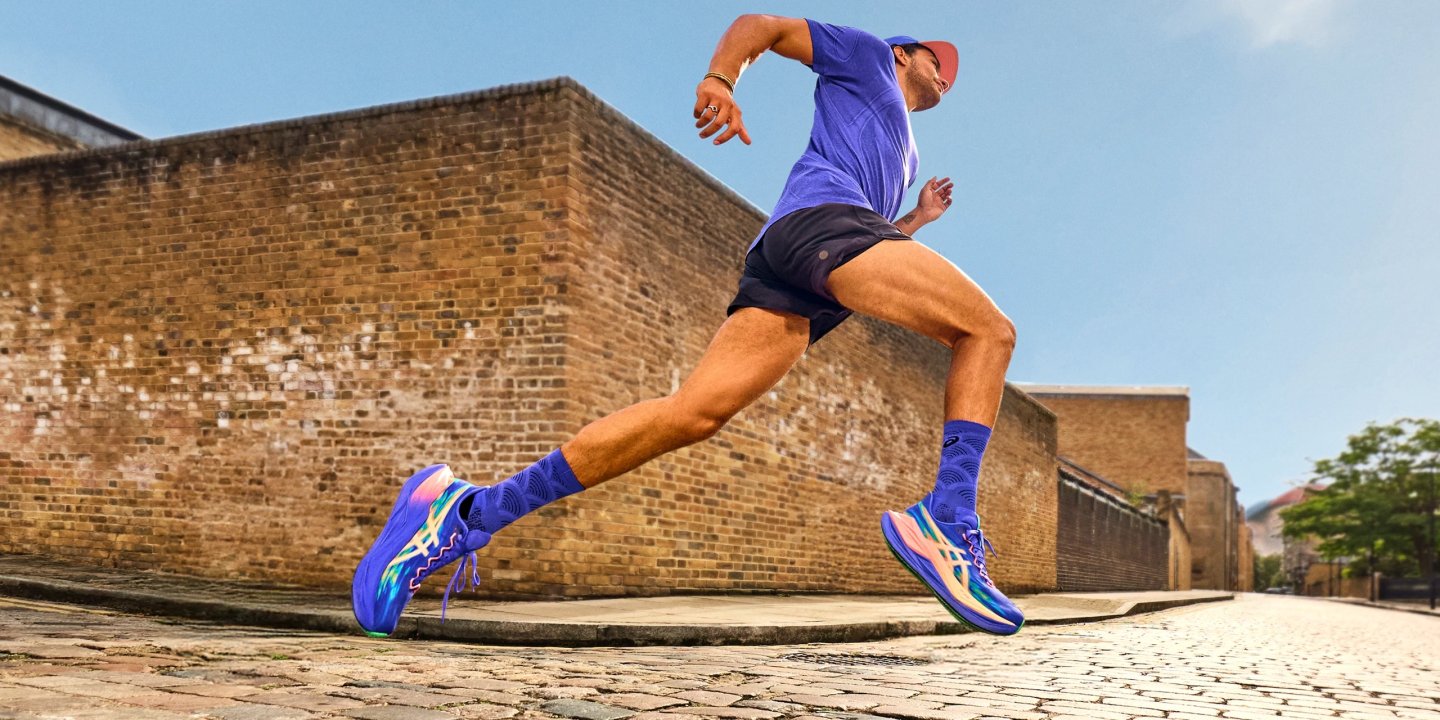 Man sprinting on cobblestone street wearing vibrant blue ASICS running shoes, blue socks, shorts and cap