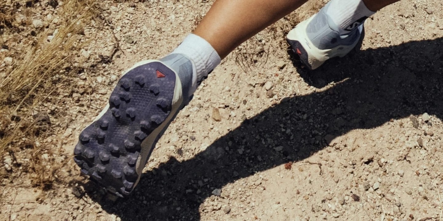 Salomon Ultra Glide 4 trail running shoe outsole showing aggressive lug pattern on dusty rocky trail path
