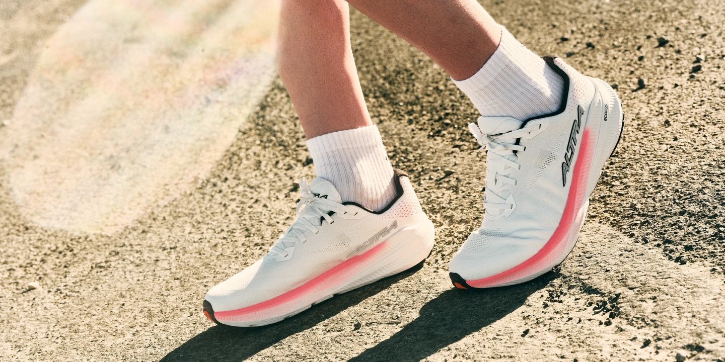 Altra Experience Flow 3 running shoes in white and coral on asphalt, side profile showing midsole cushioning and mesh upper.