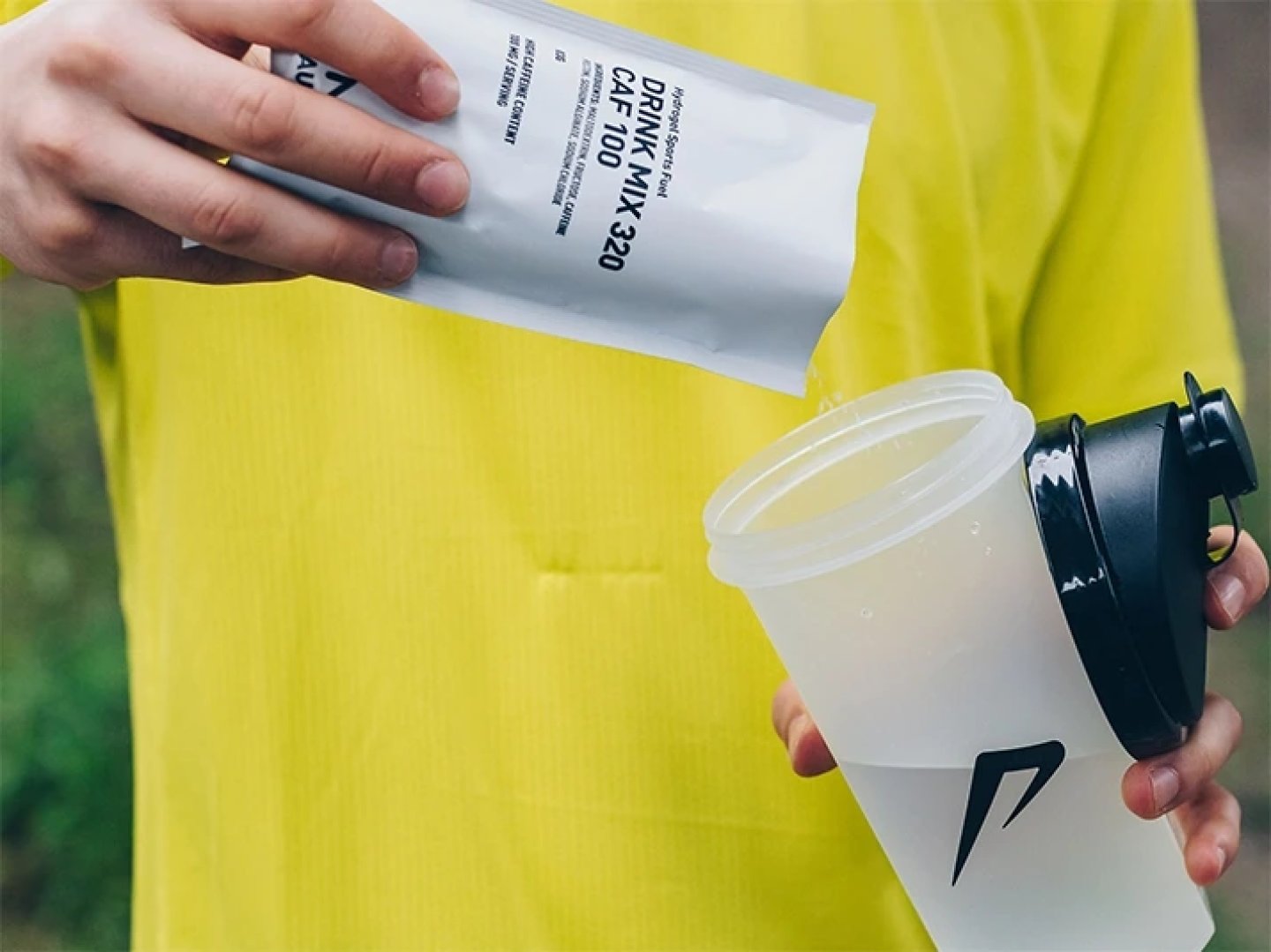 Runner in yellow jacket pouring Precision Fuel Hydration Drink Mix 320 CAF 100 sachet into a clear shaker bottle