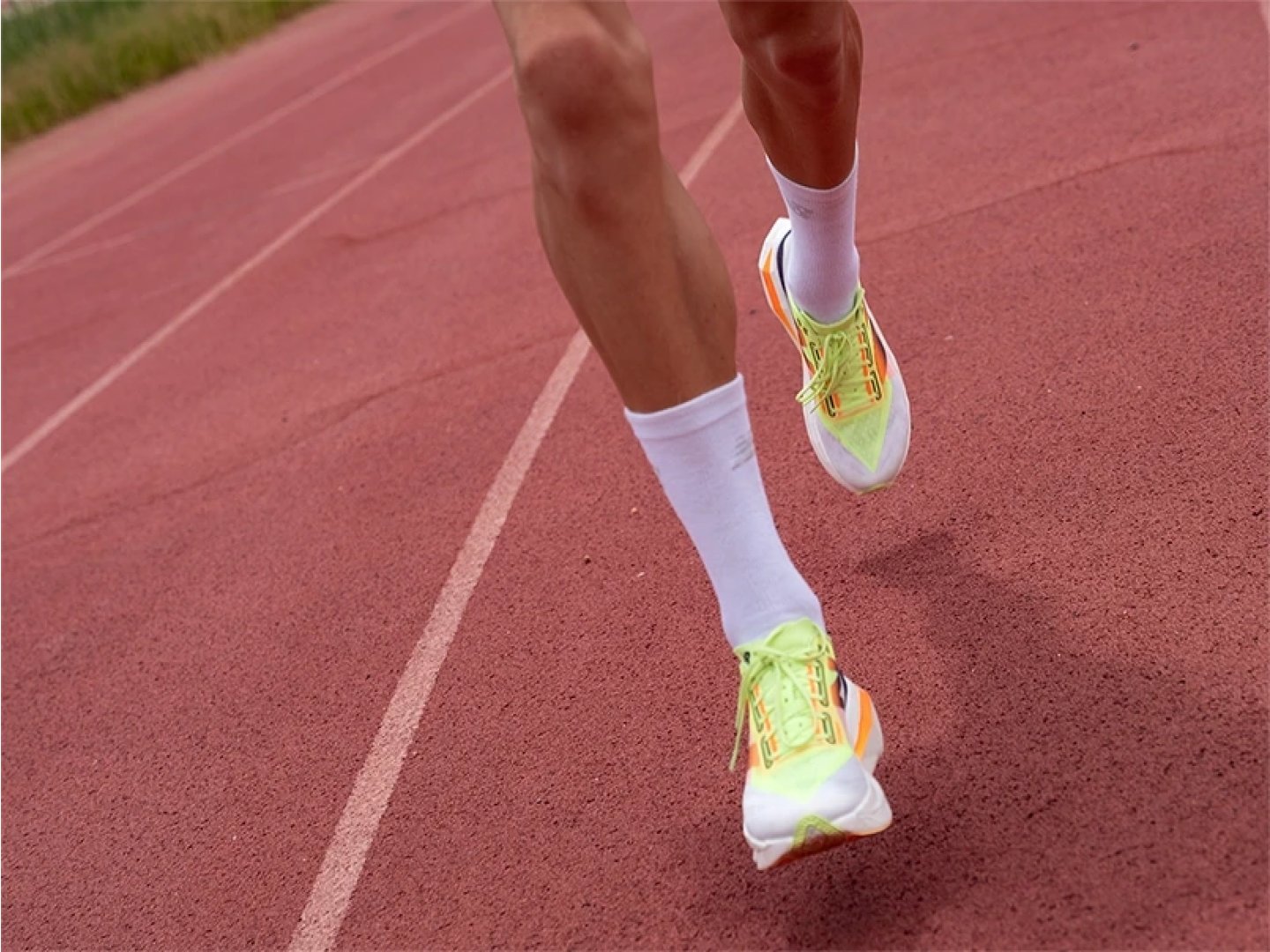Side view of a runner's legs in neon yellow-green racing shoes sprinting on a red running track during interval training.