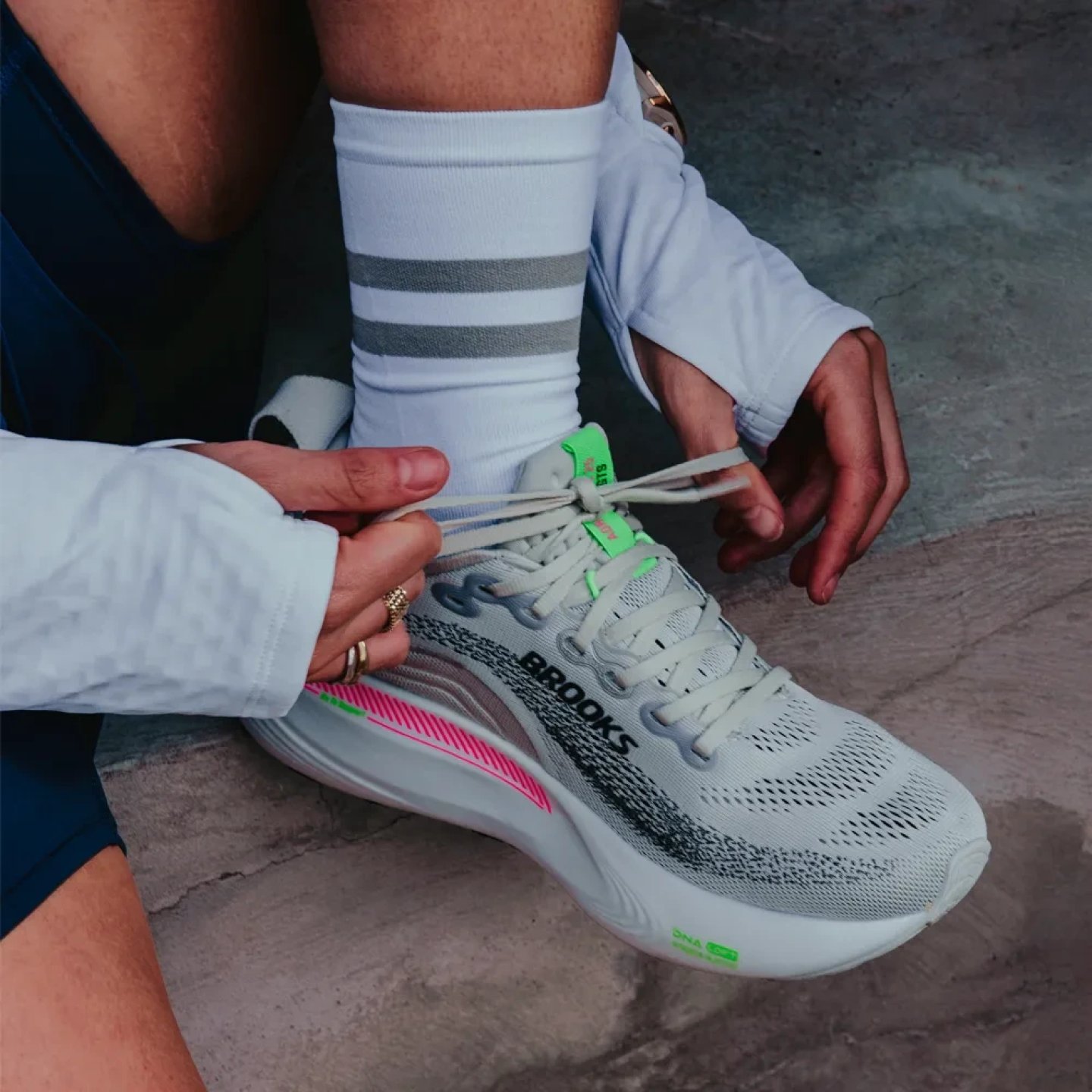 Person tying laces on a Brooks Adrenaline stability running shoe in grey with pink and green accents