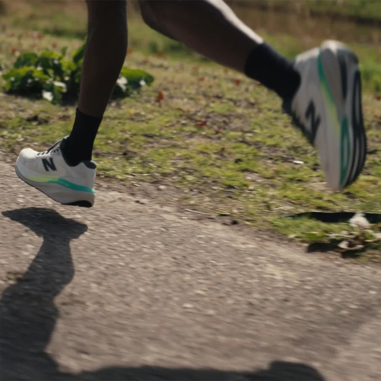 Close-up of runner's feet in white and teal New Balance running shoes on a paved path, demonstrating overpronation gait.