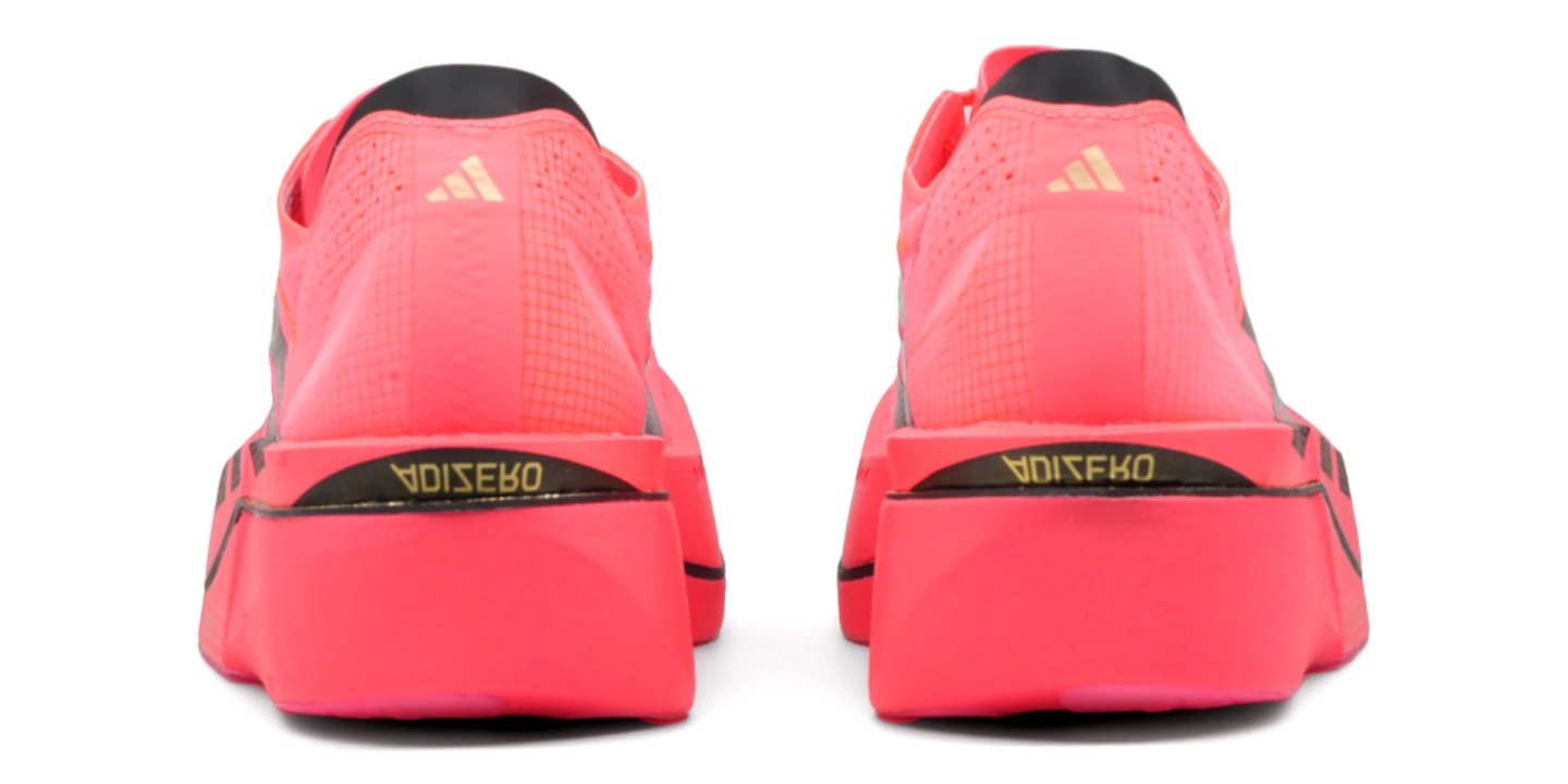 Rear view of a pair of Adidas Adizero Adios Pro 5 running shoes in coral pink with black and gold midsole branding.