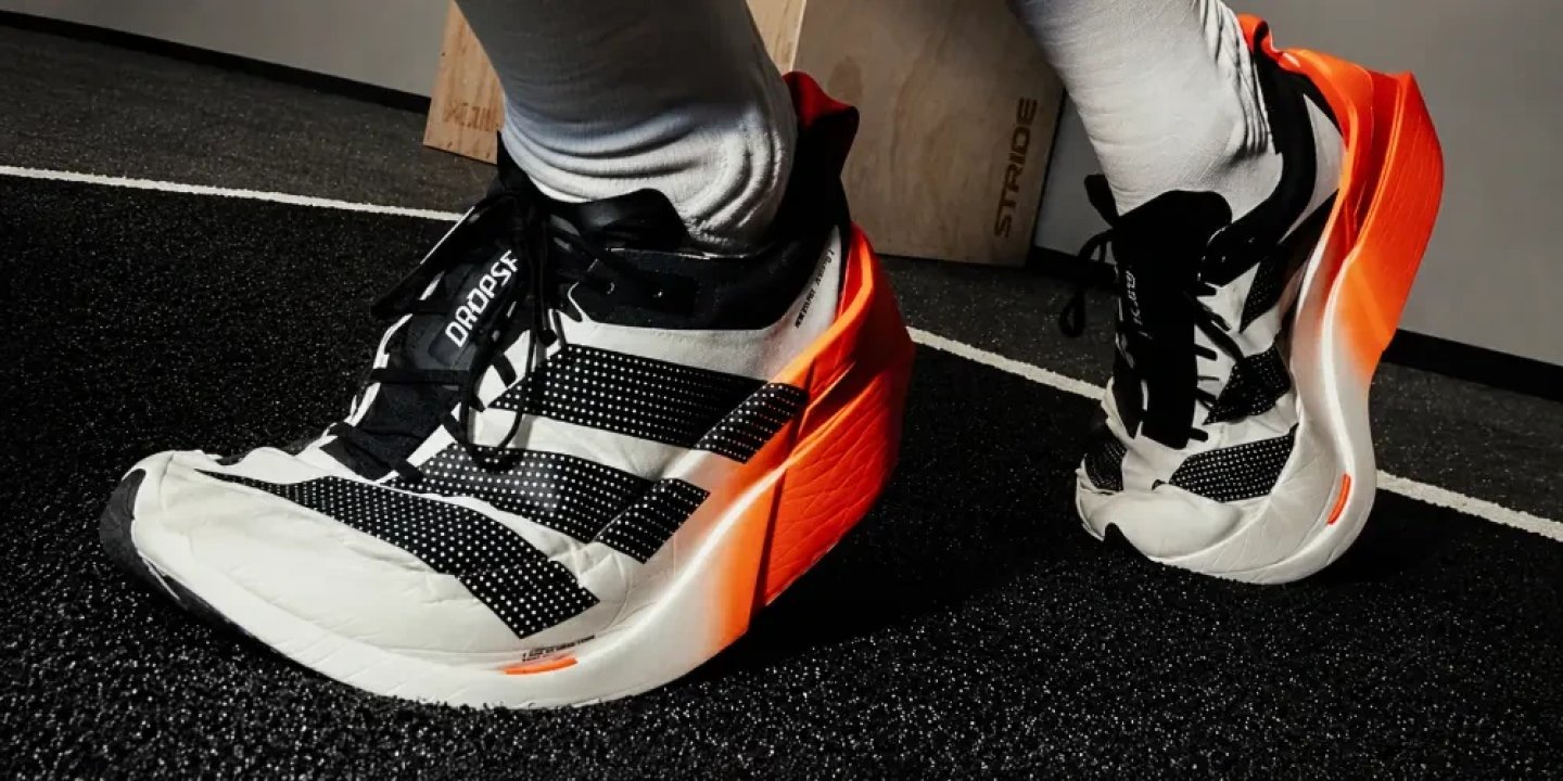 Adidas Adizero Dropset Elite running shoes in white, black, and orange, worn on a gym track surface