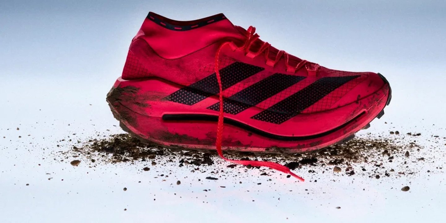 Adidas Terrex Agravic Speed Evo trail running shoe in red and black, shown with mud and dirt on a studio background.
