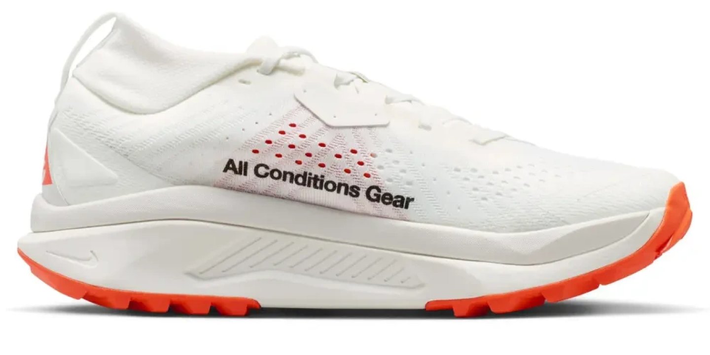 Nike ACG Zegama trail running shoe in white with orange outsole and All Conditions Gear branding on the lateral side.
