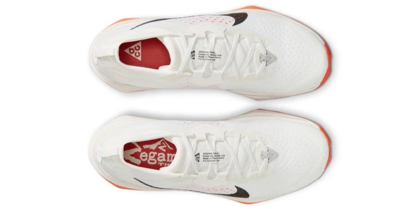 Nike ACG Zegama trail running shoes seen from above, white knit upper with black Swoosh and orange midsole trim, pair shown