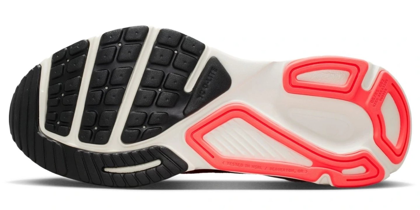 Bottom view of Nike running shoe outsole showing black XC-Lite rubber lugs and coral pink heel traction pod on white midsole
