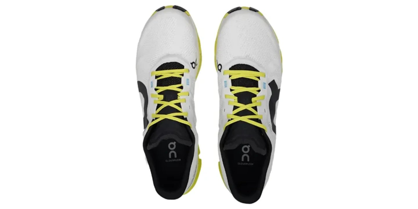 Top view of On Cloudflow running shoes in white and black with neon yellow laces on white background