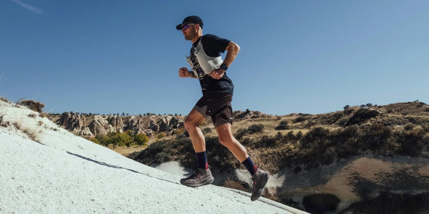 Male trail runner wearing Salomon GRVL Concept shoes running uphill on white rock terrain in Cappadocia, clear blue sky