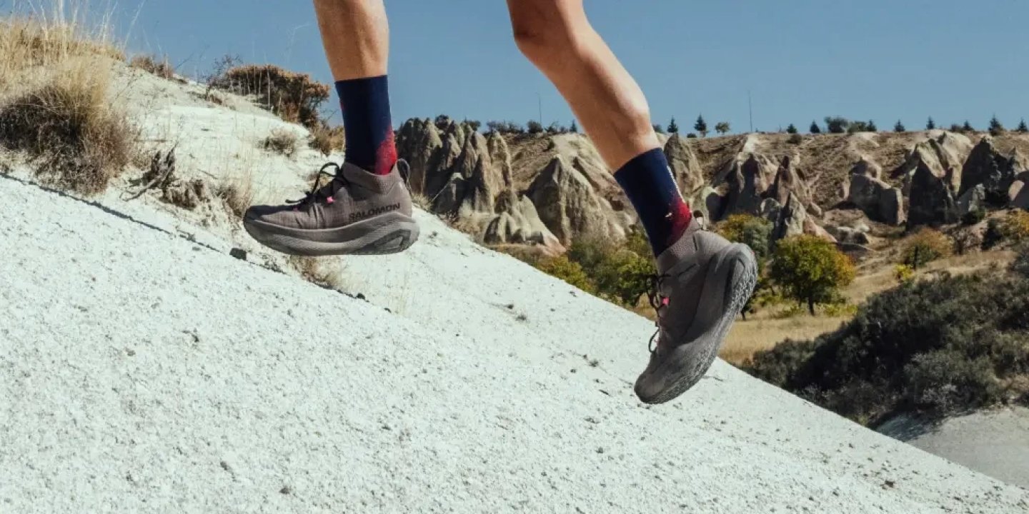 Runner wearing Salomon GRVL Concept trail running shoes ascending a rocky white stone slope with dramatic rock formations behind.