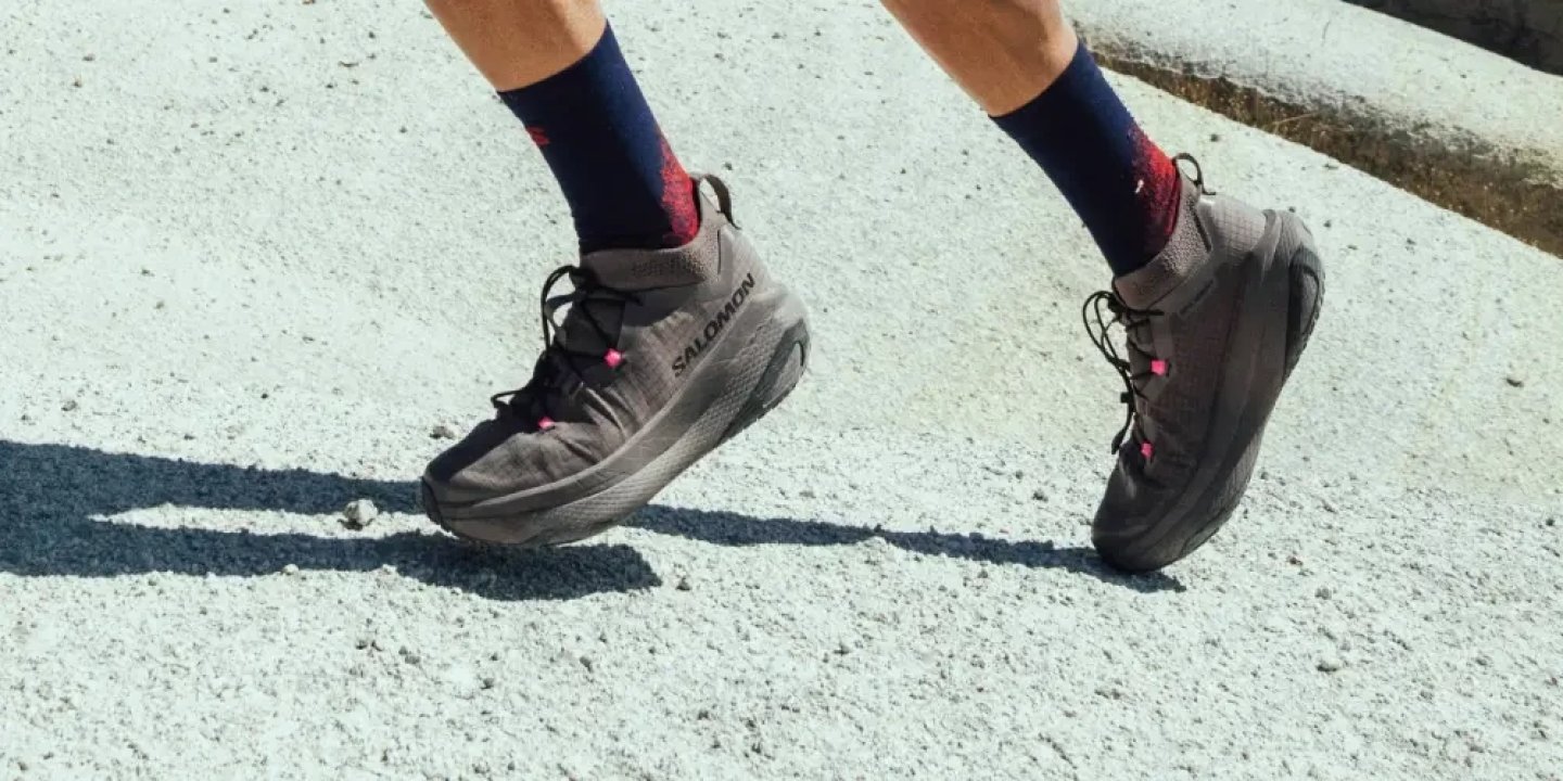 Close-up of a runner wearing Salomon GRVL Concept trail running shoes in dark grey with pink accents on a gravel surface