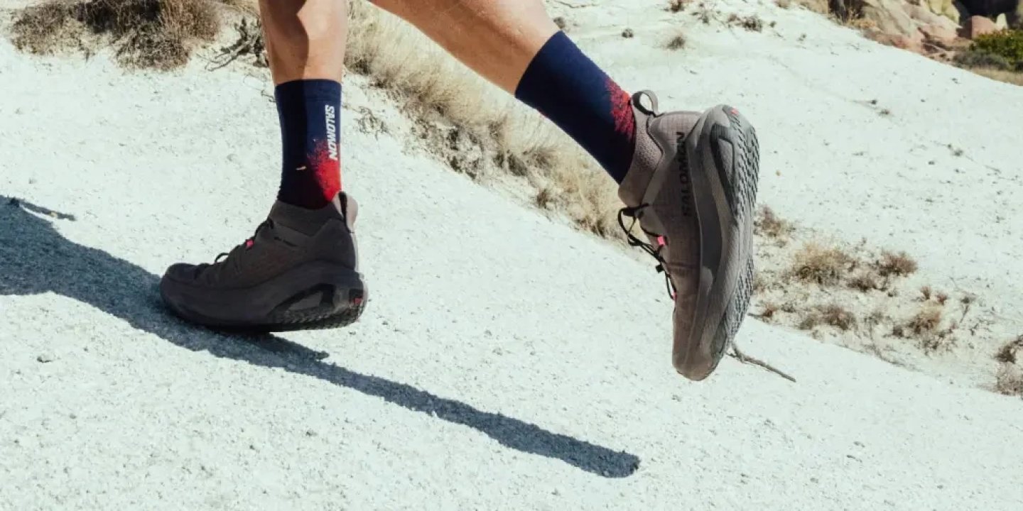 Runner wearing Salomon GRVL Concept trail running shoes and Salomon socks on a rocky, sandy trail surface.