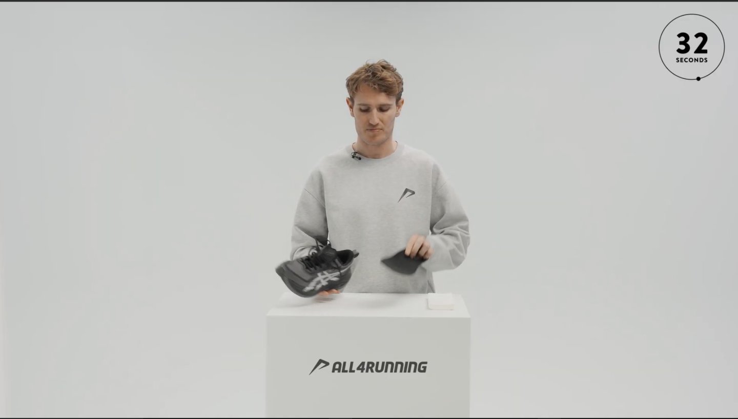 Hardloopexpert houdt een zwarte hardloopschoen vast met inlegzool eruit op een witte sokkel