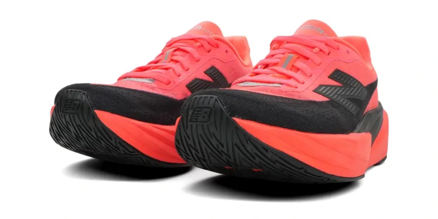 Pair of New Balance FuelCell Rebel V4 running shoes in neon coral and black, rear three-quarter view showing thick midsole