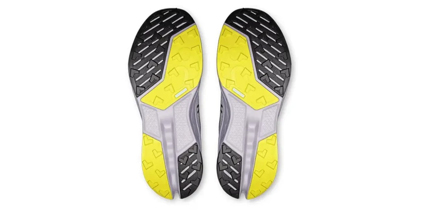 Bottom view of On Cloudsurfer Trail 2 running shoes showing black rubber lug pattern and yellow outsole zones on both feet.