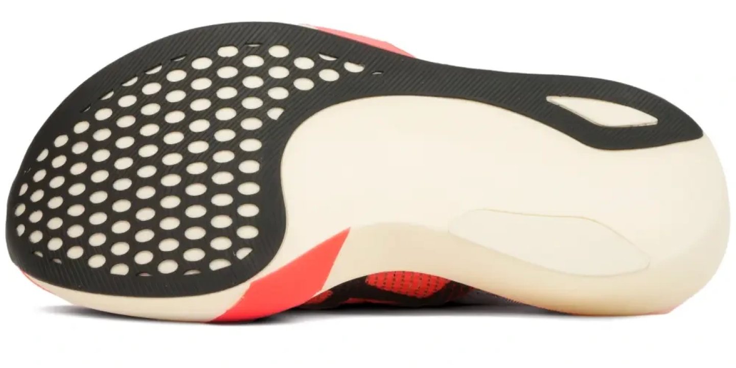 Bottom view of the Asics Metaspeed Edge Tokyo running shoe showing perforated black rubber outsole and cream midsole with coral upper details.