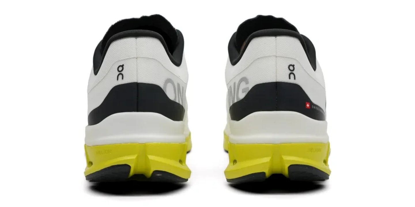 Rear view of On running shoes in white and black with a vibrant yellow CloudTec midsole and Swiss flag badge