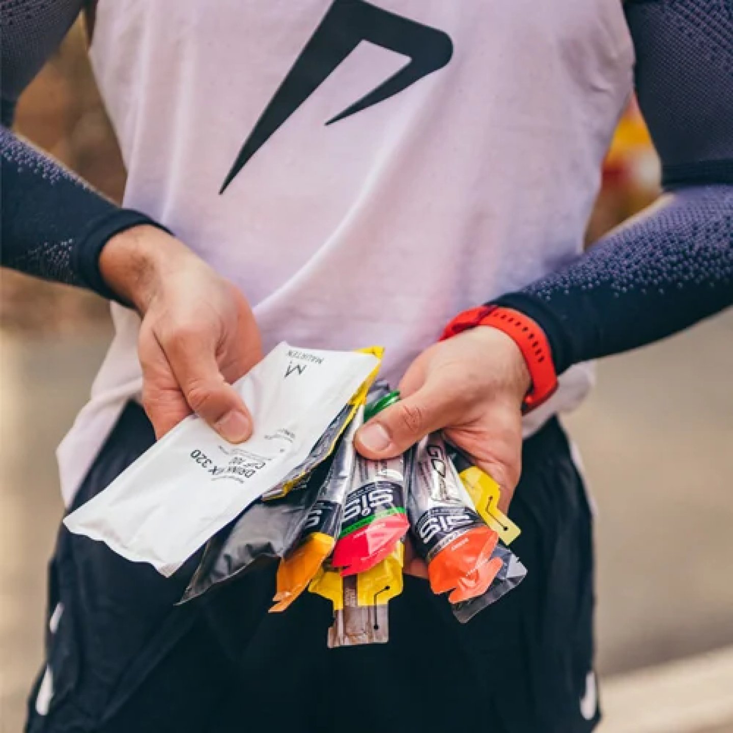 Athlete holding a bundle of SiS energy gels in multiple flavours during a race, wearing a white running vest.