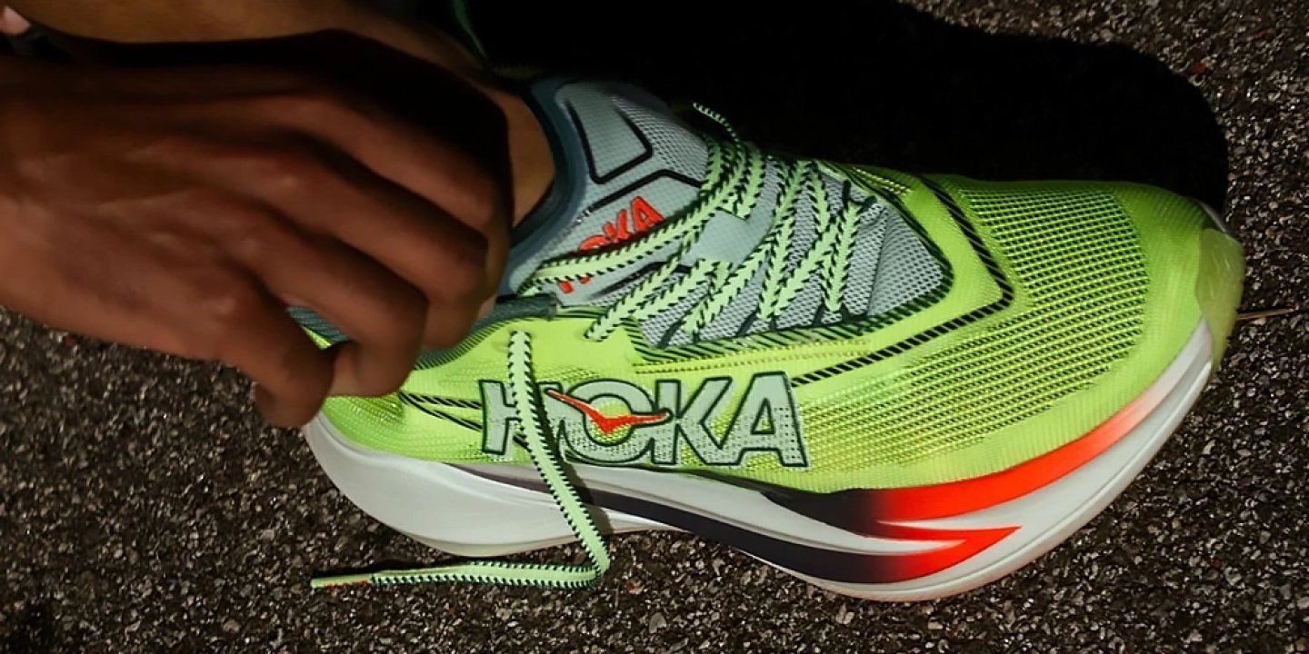 Runner lacing up the Hoka Cielo X1 3 in lime green, highlighting the engineered mesh upper and bold Hoka branding.