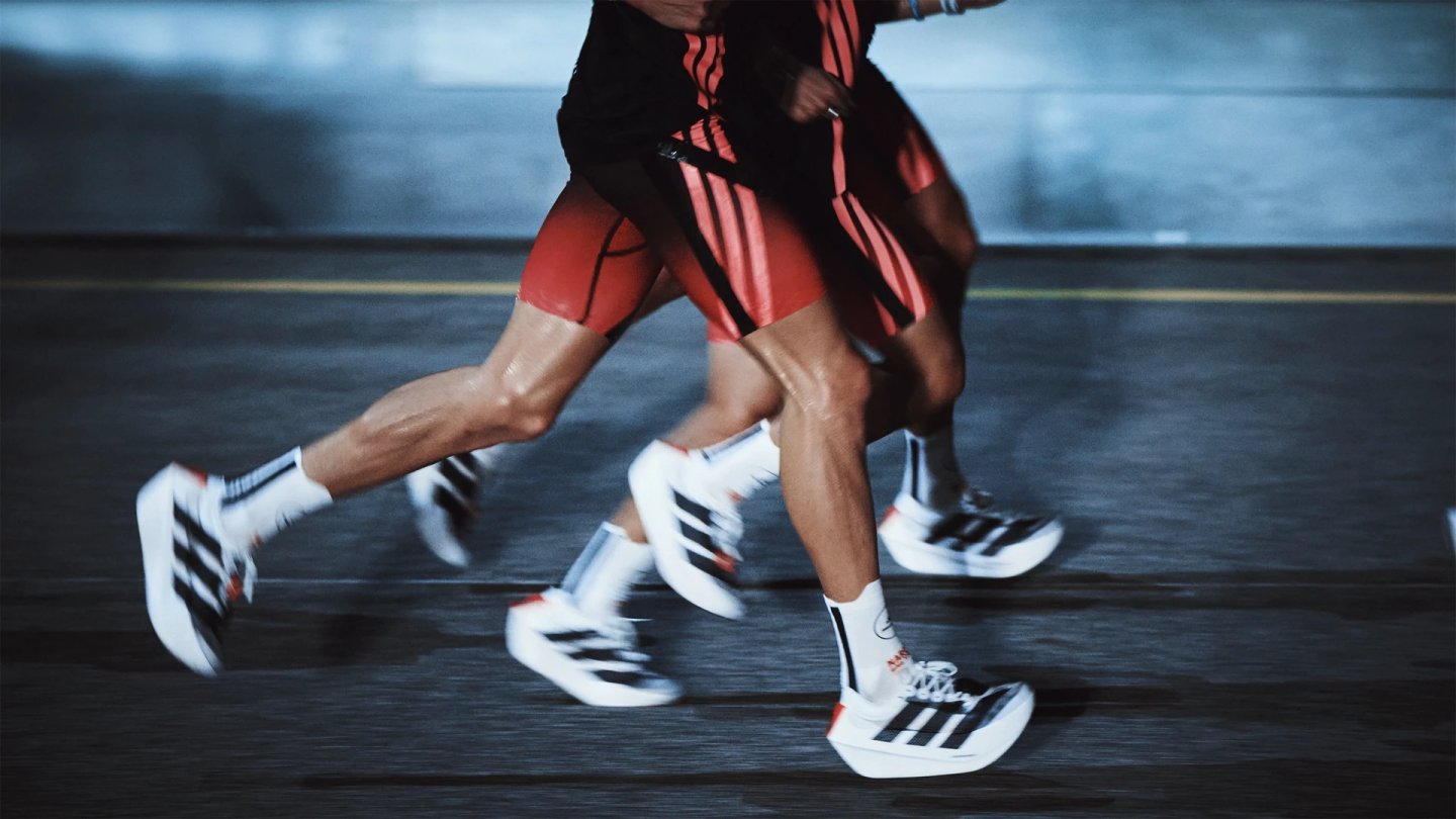 Close-up of two runners' legs mid-stride wearing white and black Adidas Adizero Prime EVO X running shoes