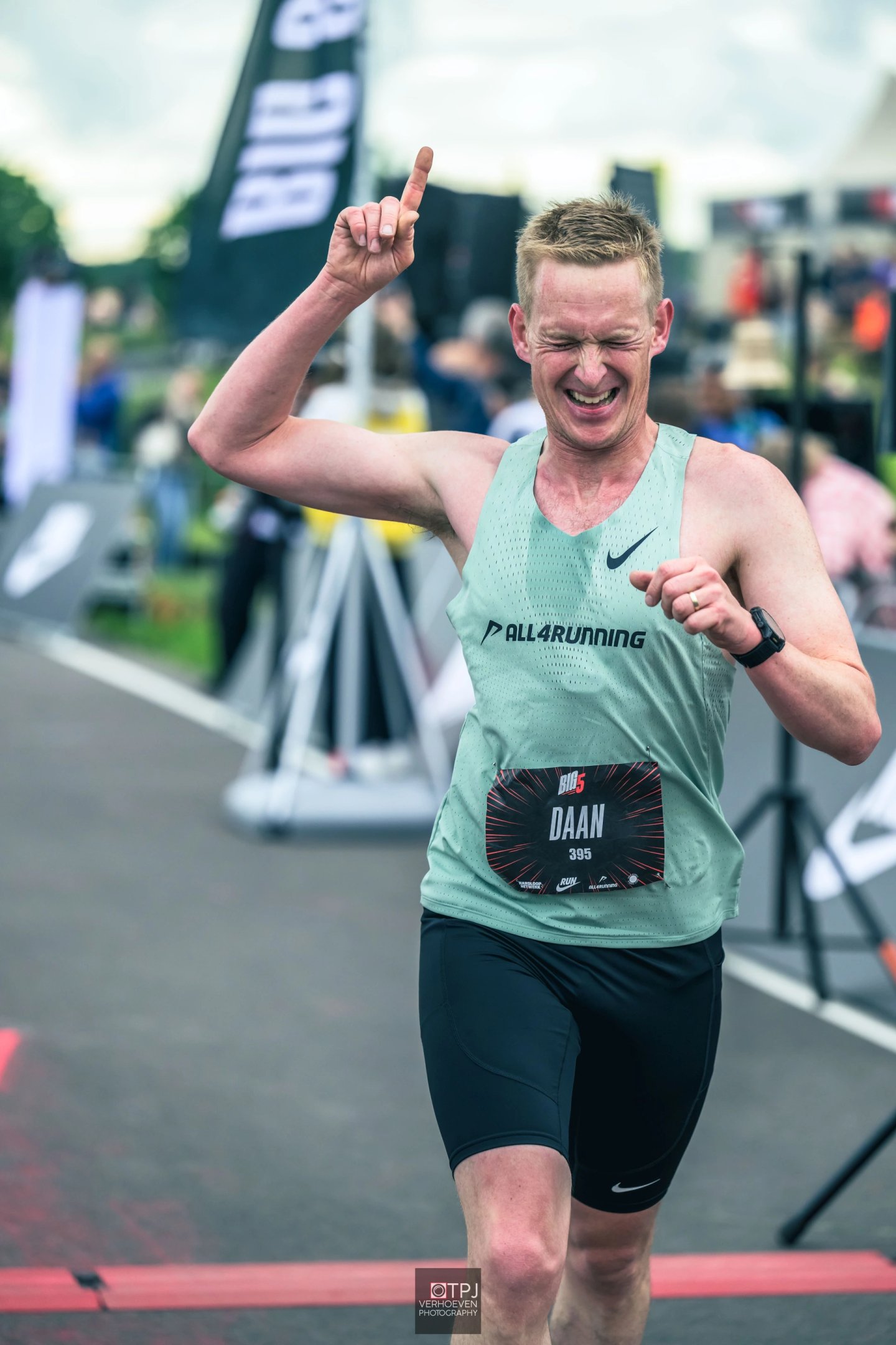 Elated male runner named Daan, bib 395, celebrating at finish line in green Nike singlet and black compression shorts.